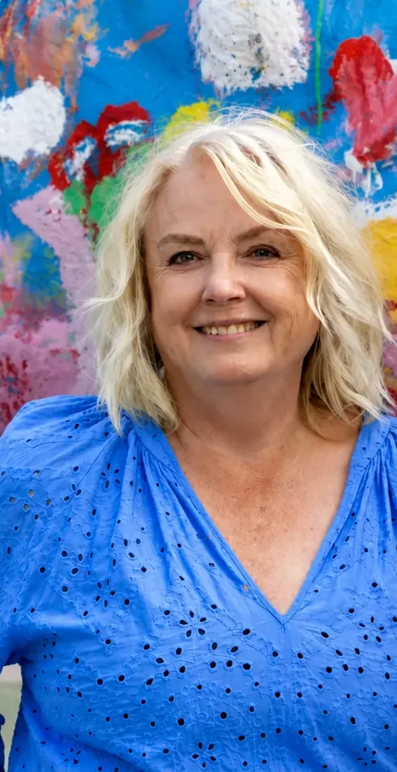 Samtalsterapeut Madeleine Bengtson i blå blus ler framför en färgglad målad vägg